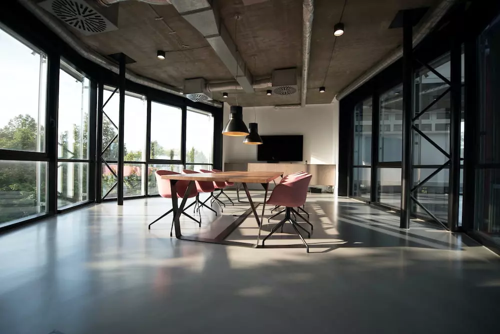 Modern office meeting room with a wooden table, pink chairs, and large windows.