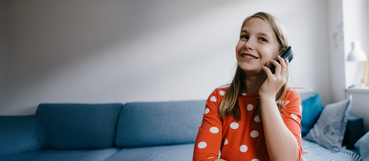 A young girl with blonde hair smiling and holding a black cordless home phone to her ear suggesting the value of having a home phone