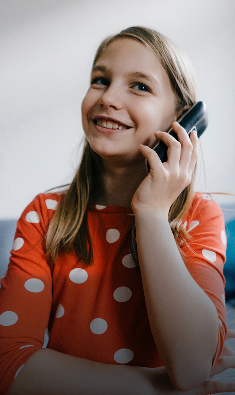 A young girl with blonde hair smiling and holding a black cordless home phone to her ear suggesting the value of having a home phone