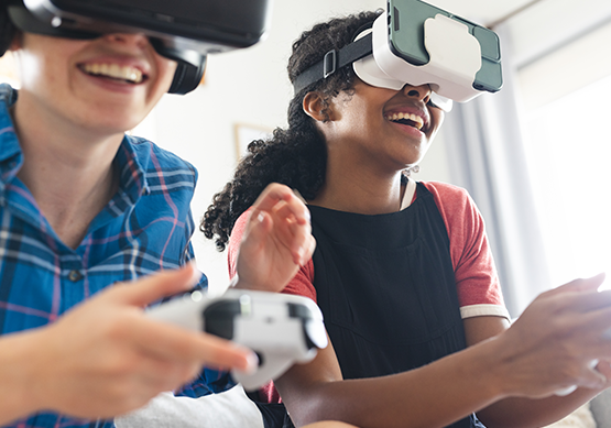 Two friends wearing virtual reality headsets play an immersive VR game together while holding controllers and smiling indoors using Optimum Fiber 