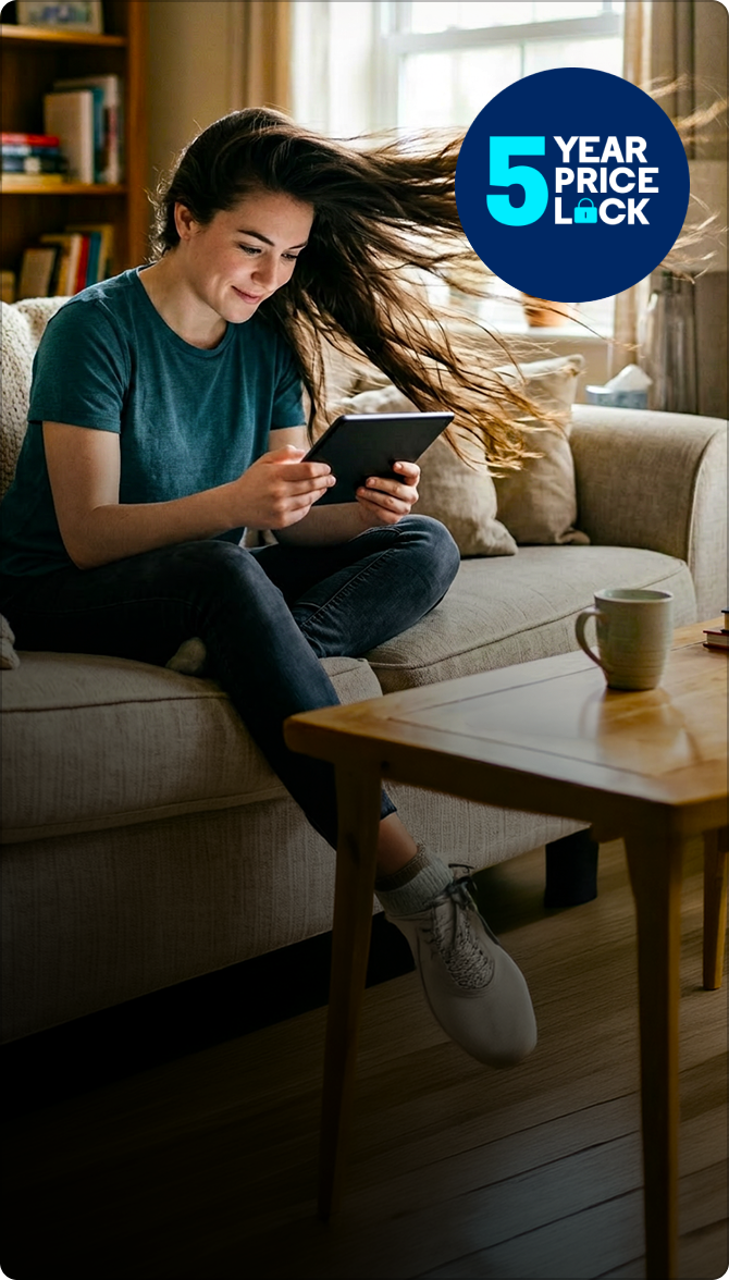 Woman with long flowing hair sits on a sofa looking at a tablet, smiling; coffee mug and books on the table