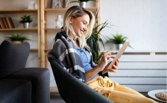Woman in cream sweater on grey sofa raising hands at open laptop on coffee table