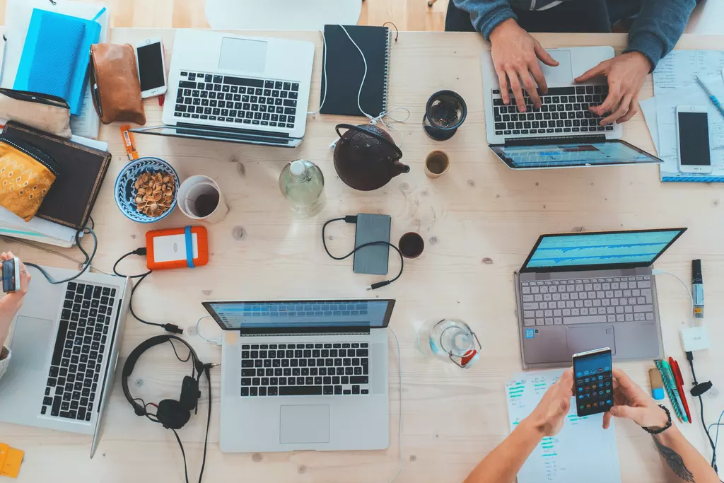 Top-down view of people working on laptops and smartphones at a shared wooden table.