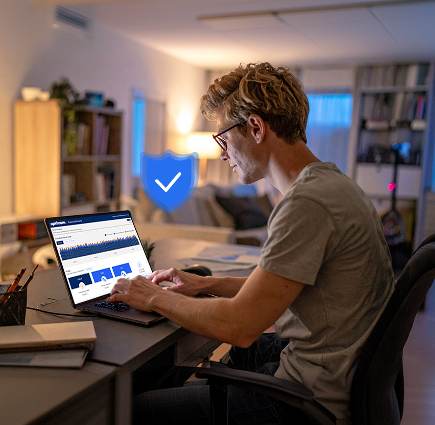 Man in glasses working on a laptop at a desk with a blue shield checkmark graphic beside him
