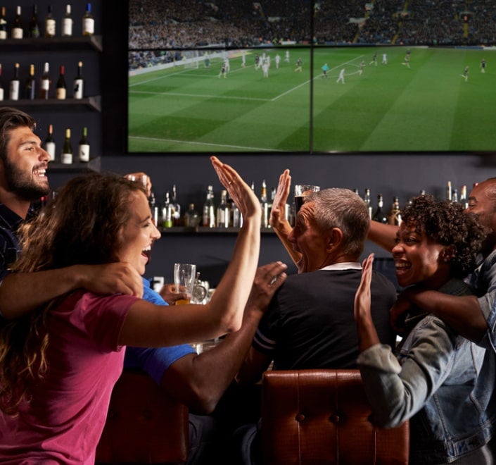 Imagen que muestra a un grupo de amigos disfrutando de un evento deportivo en un bar, utilizada para la sección del paquete de programas deportivos de Optimum Business.