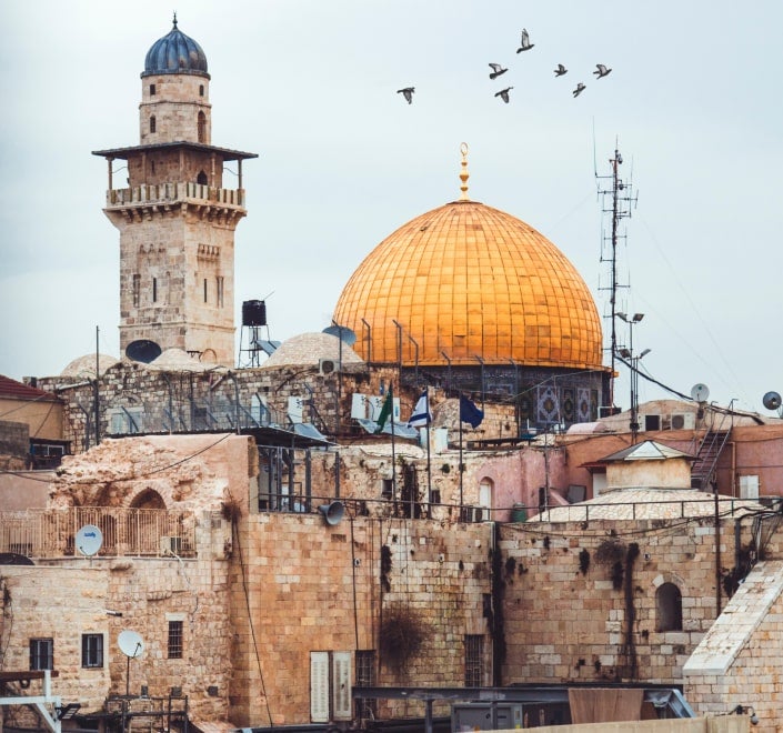 Vista de la Cúpula de la Roca en Jerusalén, rodeada de arquitectura histórica y con aves volando sobre ella.