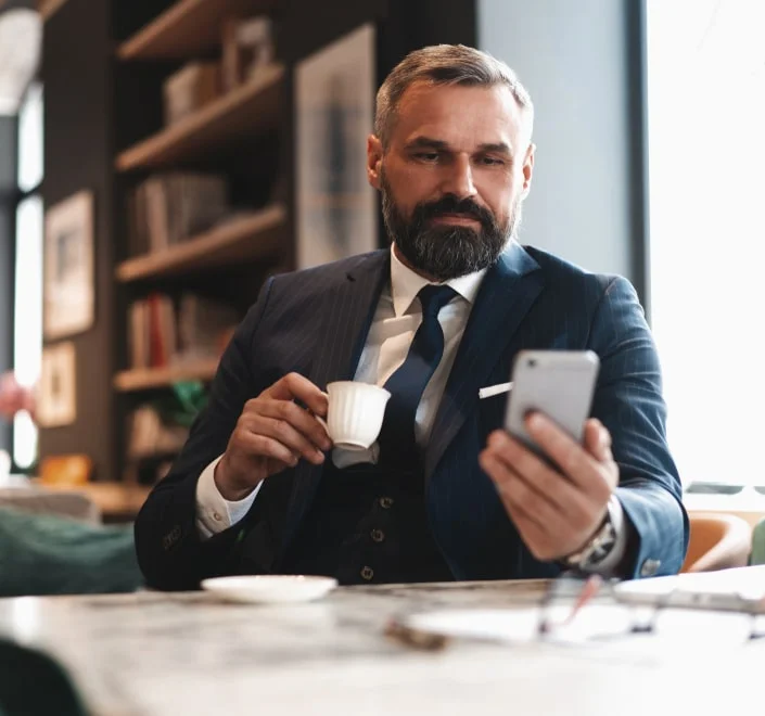 Un hombre de negocios toma café mientras usa el teléfono