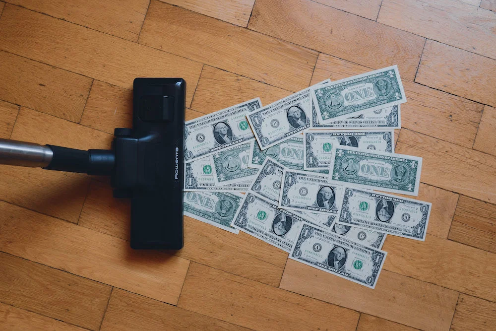 Vacuum cleaner vacuuming up dollar bills.