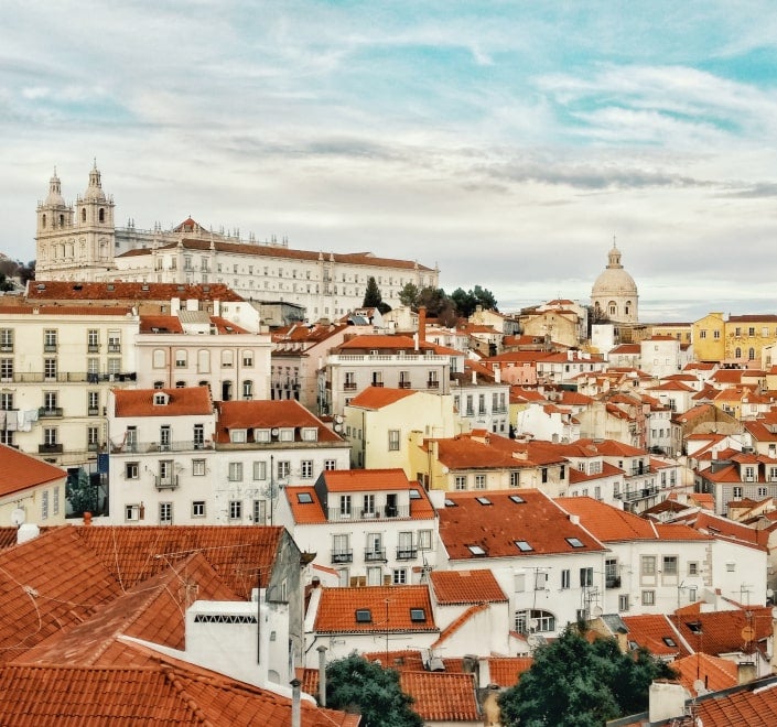 Imagen de una tarjeta que muestra el paisaje urbano de Lisboa con sus característicos tejados rojos, probablemente utilizada por un canal de televisión portugués.