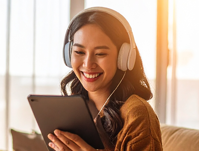 Woman wearing headphones smiles while watching content on a tablet at home, enjoying online entertainment or streaming media with Optimum Fiber 