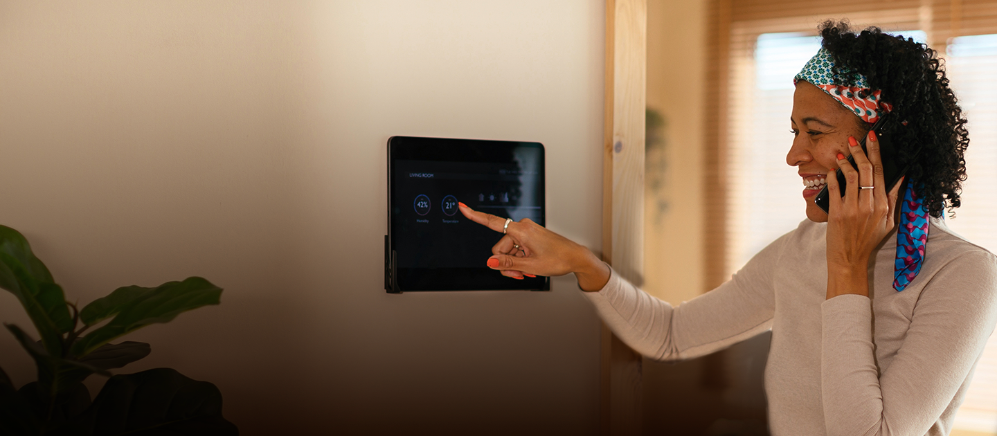 A young woman is seen pointing to a sleek black smart home hub, the screen shows icons and what appears to be a user interface. She is holding a smartphone with text that reads "Accessibility means everyone gets to connect." Below the main heading, smaller text explains that Optimum is committed to making its services accessible to all customers using Optimum Fiber Internet.