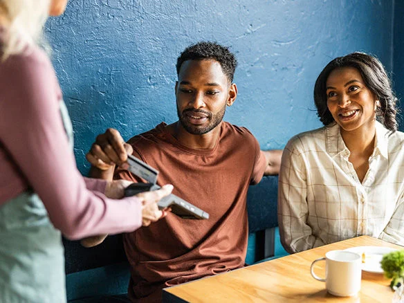 Two people exchanging a credit card payment across a restaurant table while smiling 