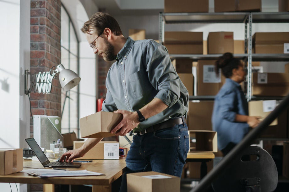 Man using a laptop for e-commerce tasks in a warehouse environment, illustrating the importance of SMB cybersecurity.