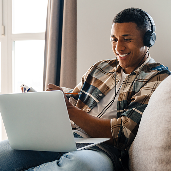 Young man with headphones smiling while using laptop at home — Optimum Advantage Internet affordable plan