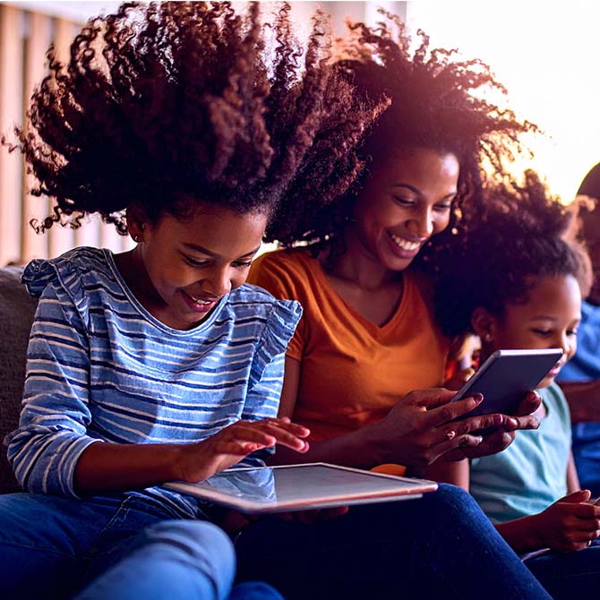 A mother and her daughters enjoying Optimum Internet on mobile phone, tablet and laptop.