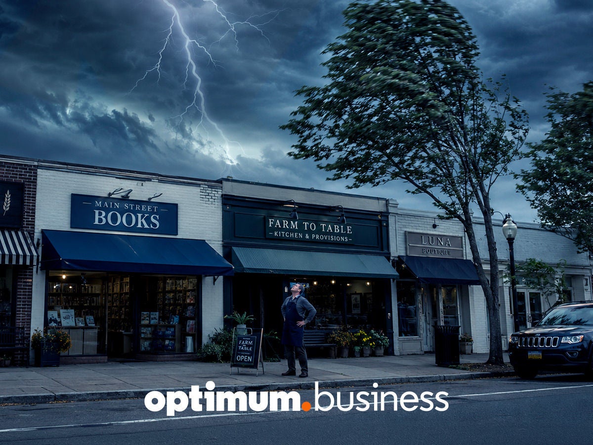 Storefronts on a Main Street stay lit during a lightning storm, representing Optimum Business backup internet keeping local shops connected.