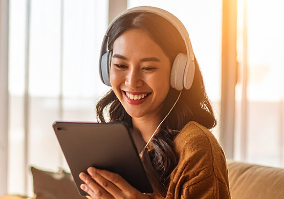 Woman wearing headphones smiles while watching content on a tablet at home, enjoying online entertainment or streaming media with Optimum Fiber 