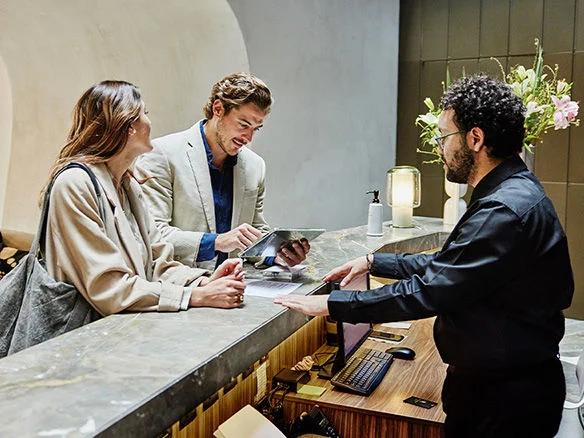 Three people in business attire reviewing documents together at a hotel front desk 
