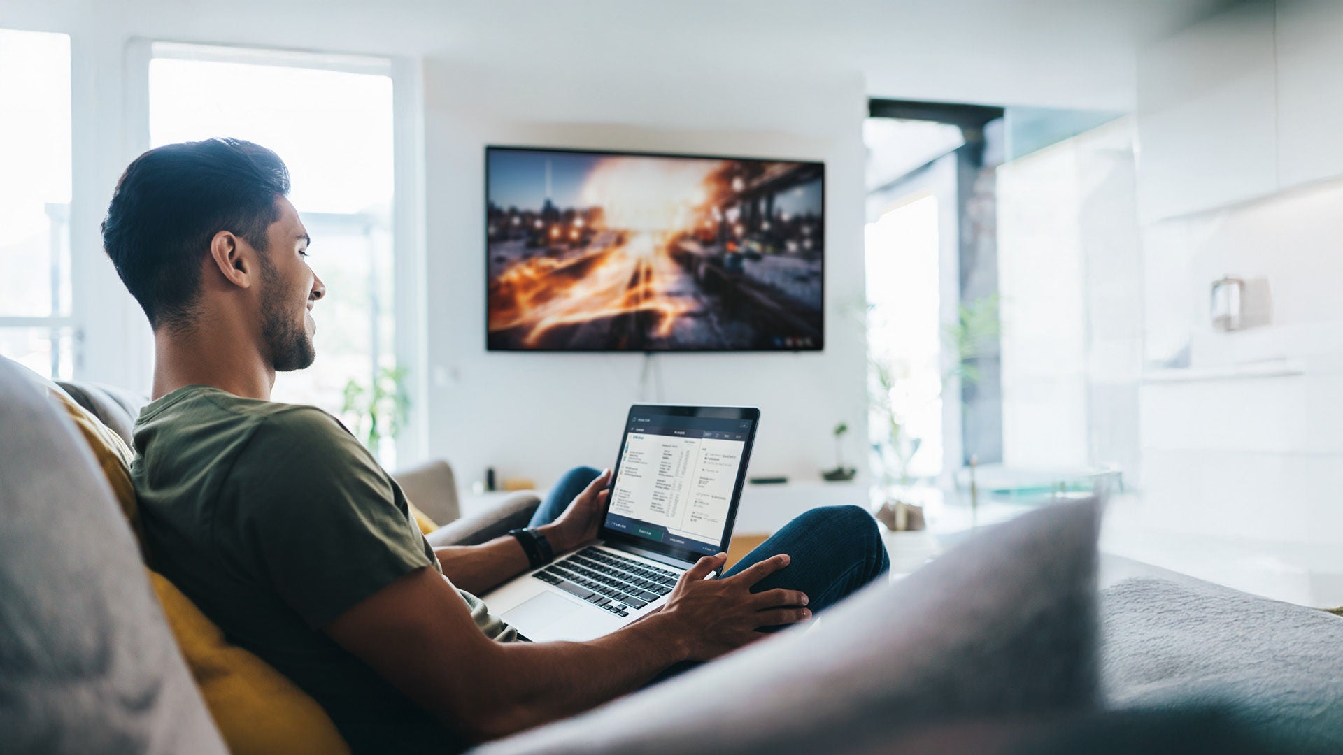 Man using high-speed Optimum home Wi-Fi on a laptop while streaming HD content on a smart TV