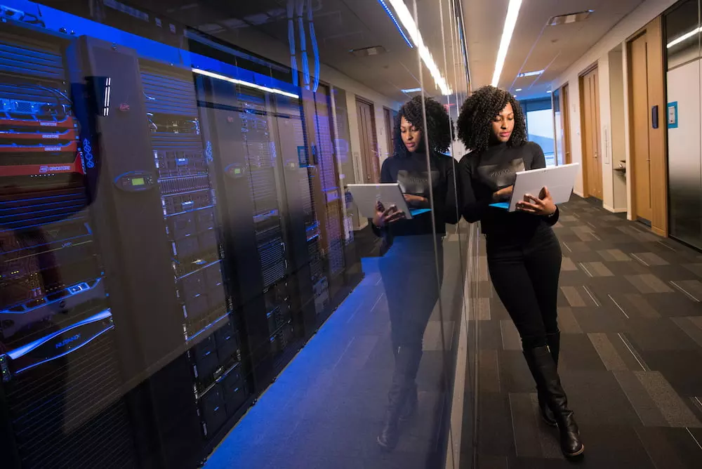 person with laptop leaning against window in front of computer system