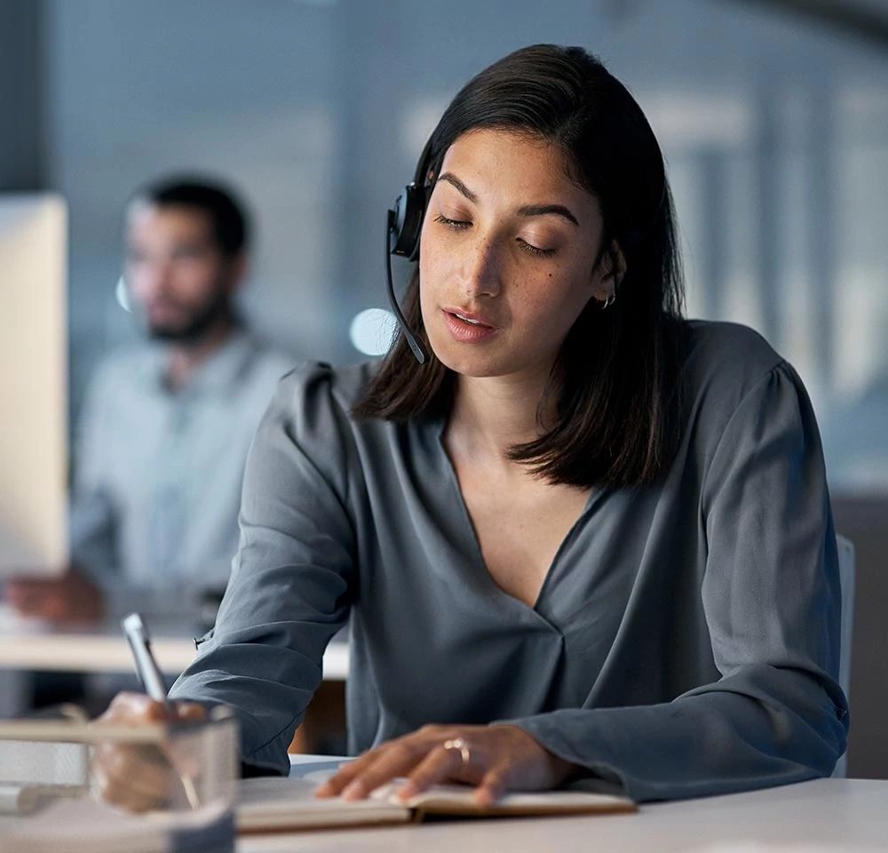 Rep at desk writing notes while wearing headset on a call