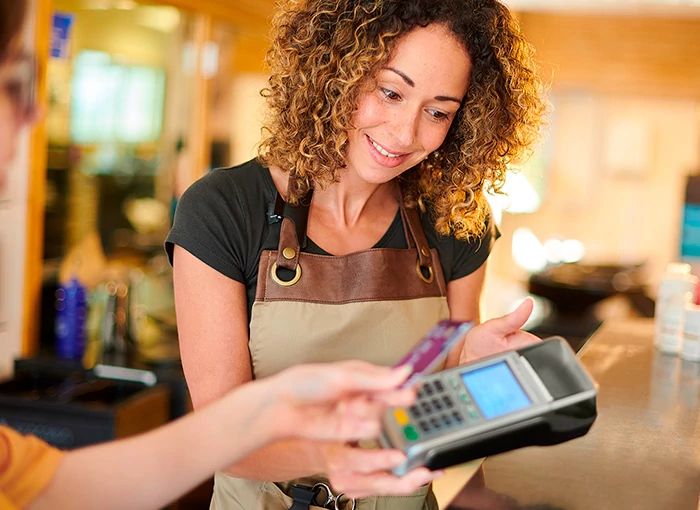 A small business owner smiles while processing a customer's credit card payment on a handheld terminal using Optimum Business Internet.