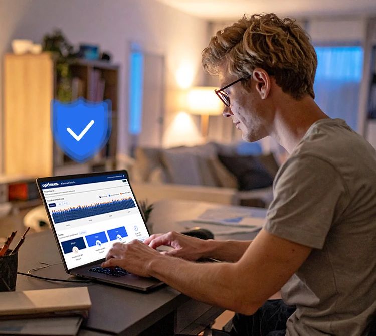 Hombre con gafas sentado en un escritorio usando una laptop en una oficina en casa, insignia azul de verificación en la esquina