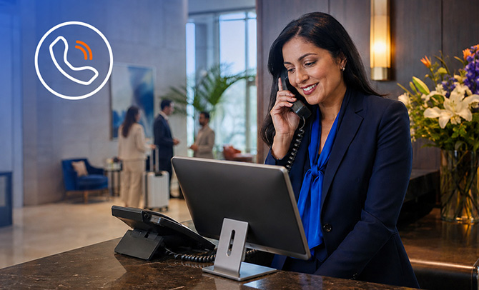 Woman on a phone call at a desk working on a laptop with a plant in the background 
