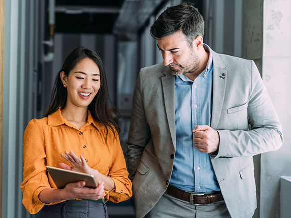 Two colleagues in business casual attire walking and talking together in a modern office hallway 