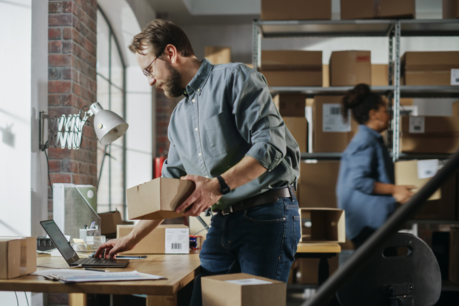 Man using a laptop for e-commerce tasks in a warehouse environment, illustrating the importance of SMB cybersecurity.
