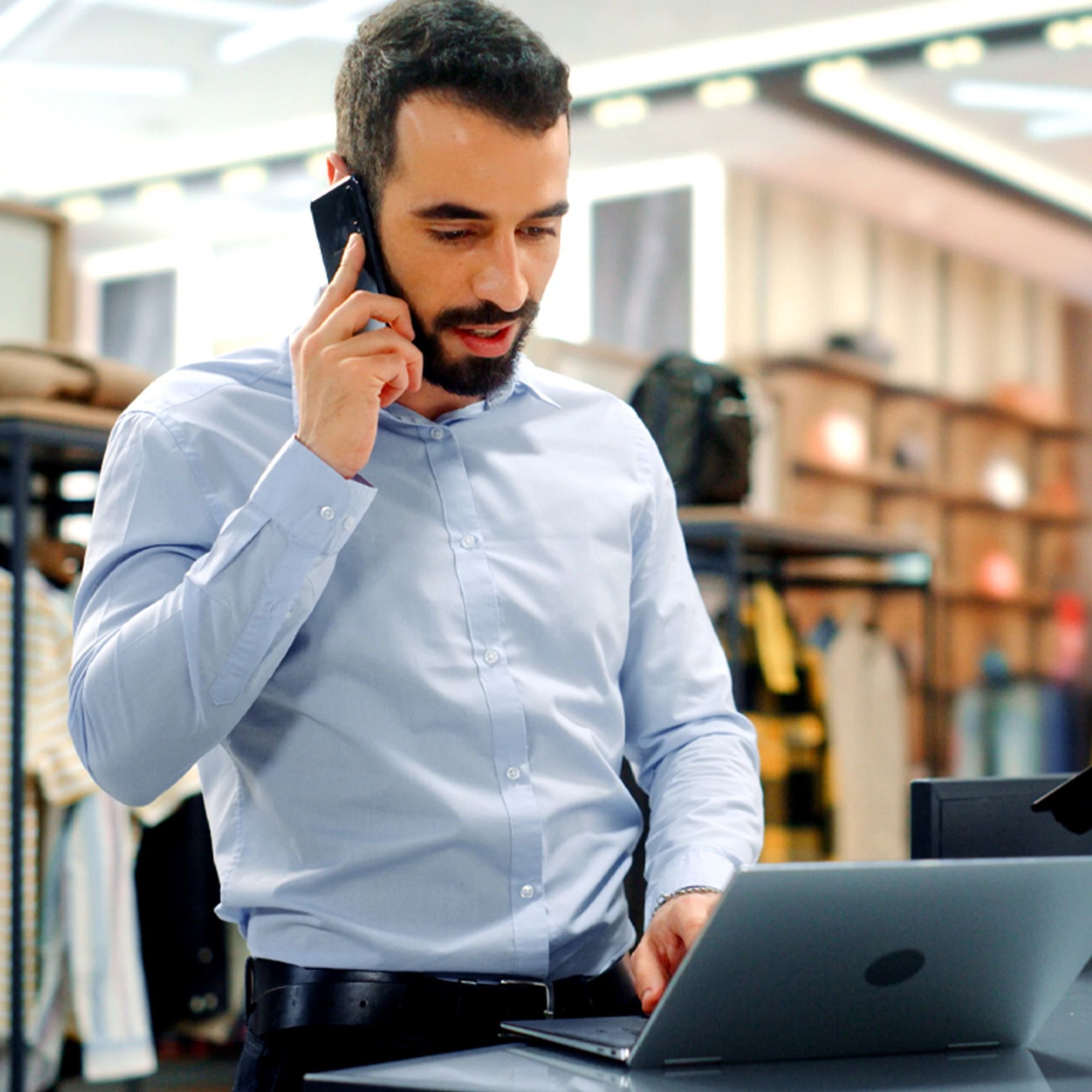 Gerente de una tienda minorista utilizando un teléfono inteligente y una computadora portátil en la caja, lo que ilustra las soluciones de conexión a Internet de alta velocidad para el comercio minorista y las empresas.