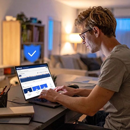 Hombre con gafas sentado en un escritorio usando una laptop en una oficina en casa, insignia azul de verificación en la esquina