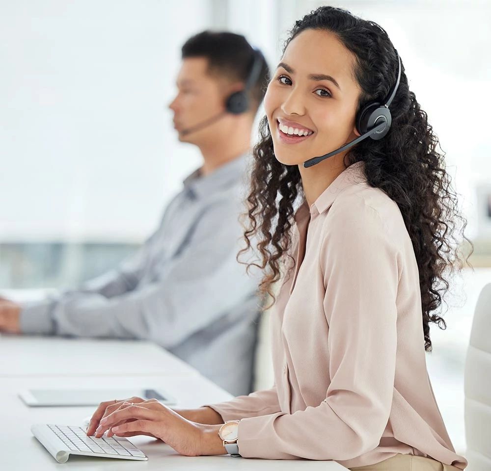 Representante sonriendo y escribiendo mientras recibe una llamada en su auricular