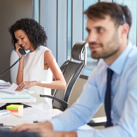 Una mujer hablando por teléfono en su escritorio con un compañero de trabajo
