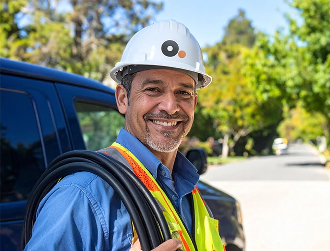 Técnico de Optimum con casco blanco y uniforme sonriendo de pie junto a una camioneta de servicio al aire libre