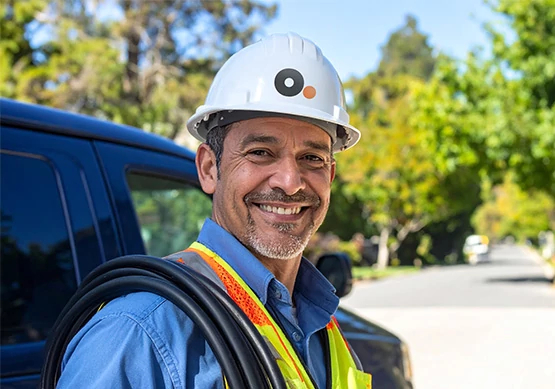 Técnico de Optimum con casco blanco y uniforme sonriendo de pie junto a una camioneta de servicio al aire libre