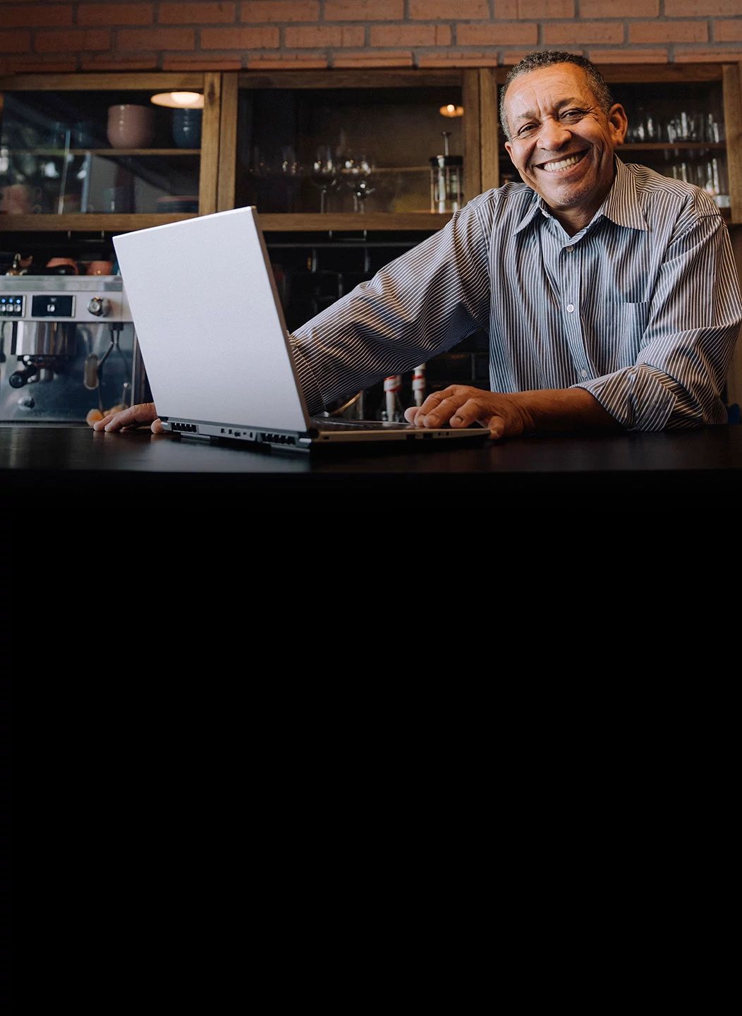 Smiling business owner using a laptop in a cafe, representing Optimum Business high-speed internet solutions.