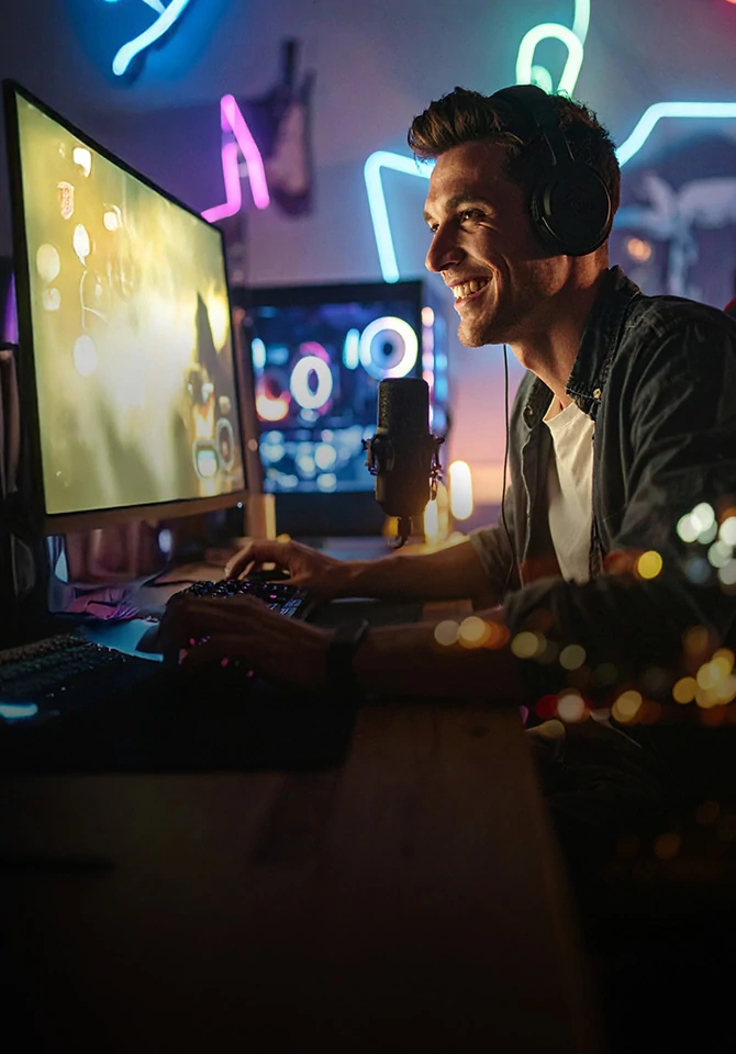 Man in headphones smiles at a glowing monitor in a gaming room lit by neon music-note signs