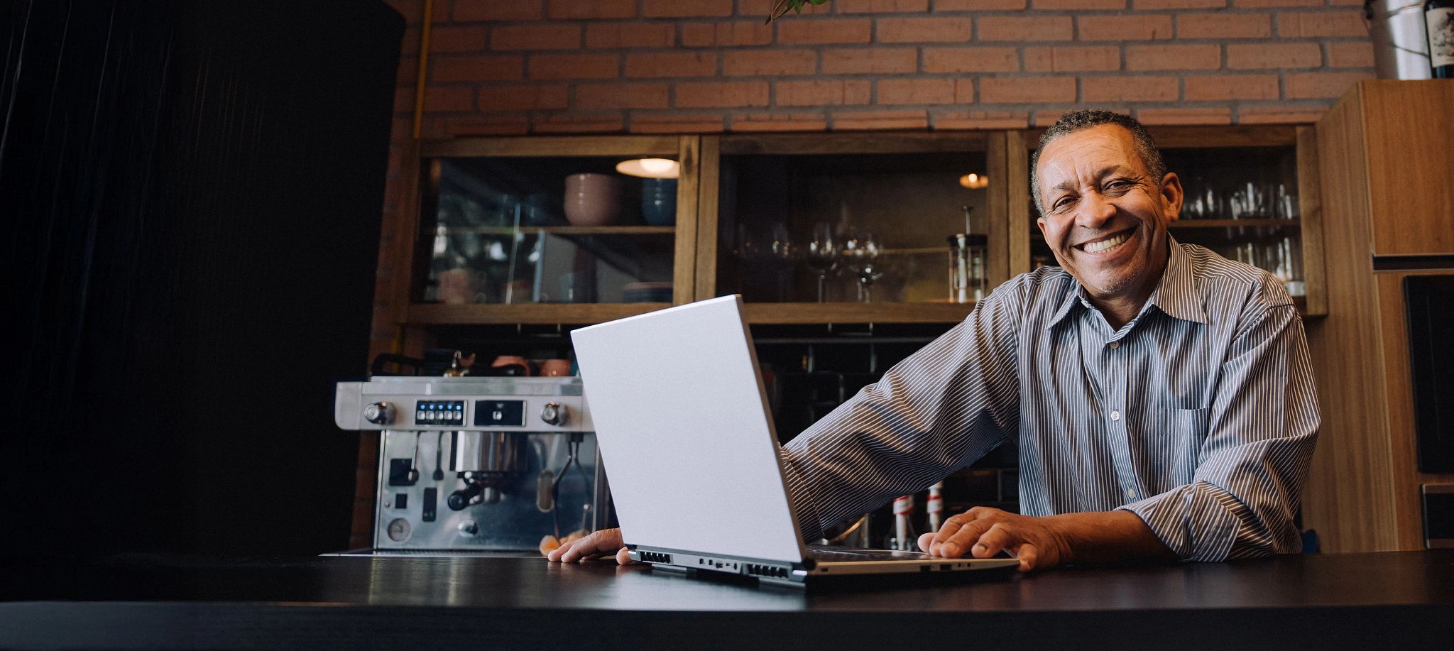 Smiling business owner using a laptop in a cafe, representing Optimum Business high-speed internet solutions.