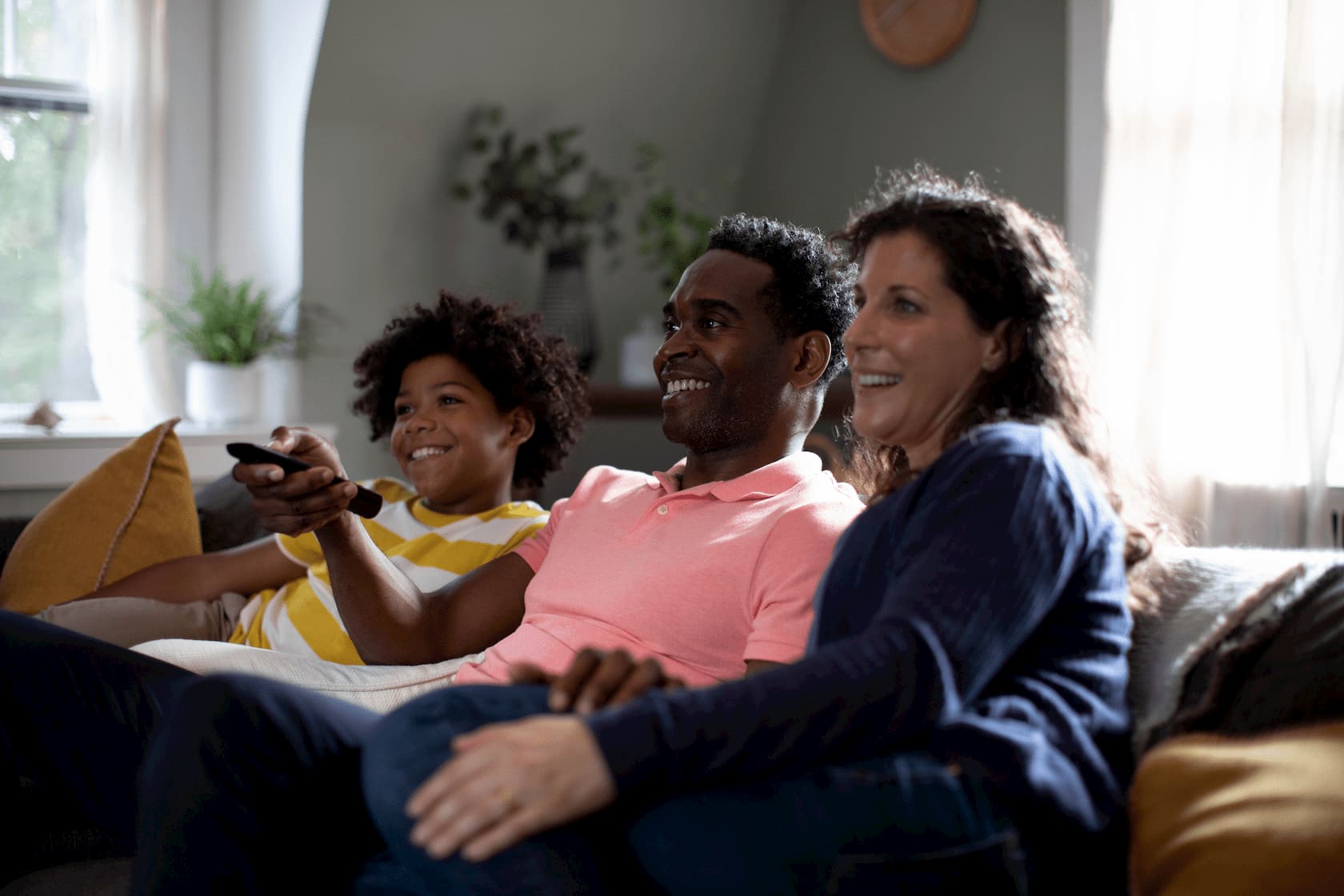 Photo of an excited family seated in a brightly lit living room, using the remote to prepare watching a movie on their home entertainment system.