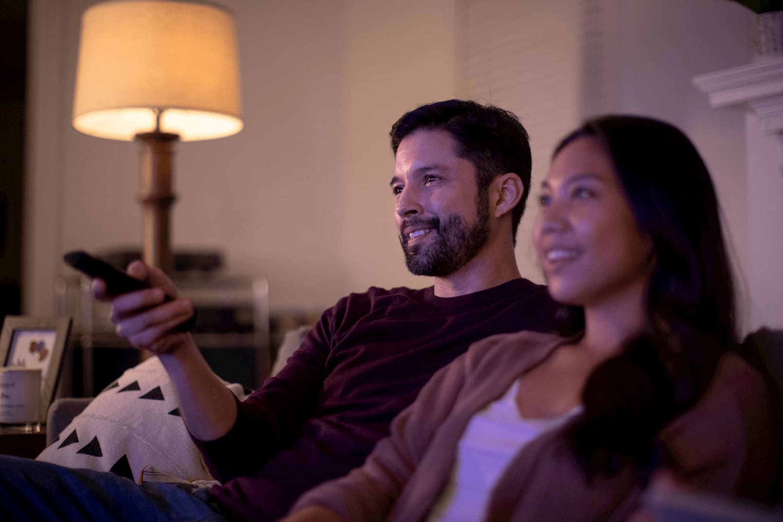 Photo of a happy couple seated in a living room, using the remote and preparing to watch a movie on their home entertainment system.