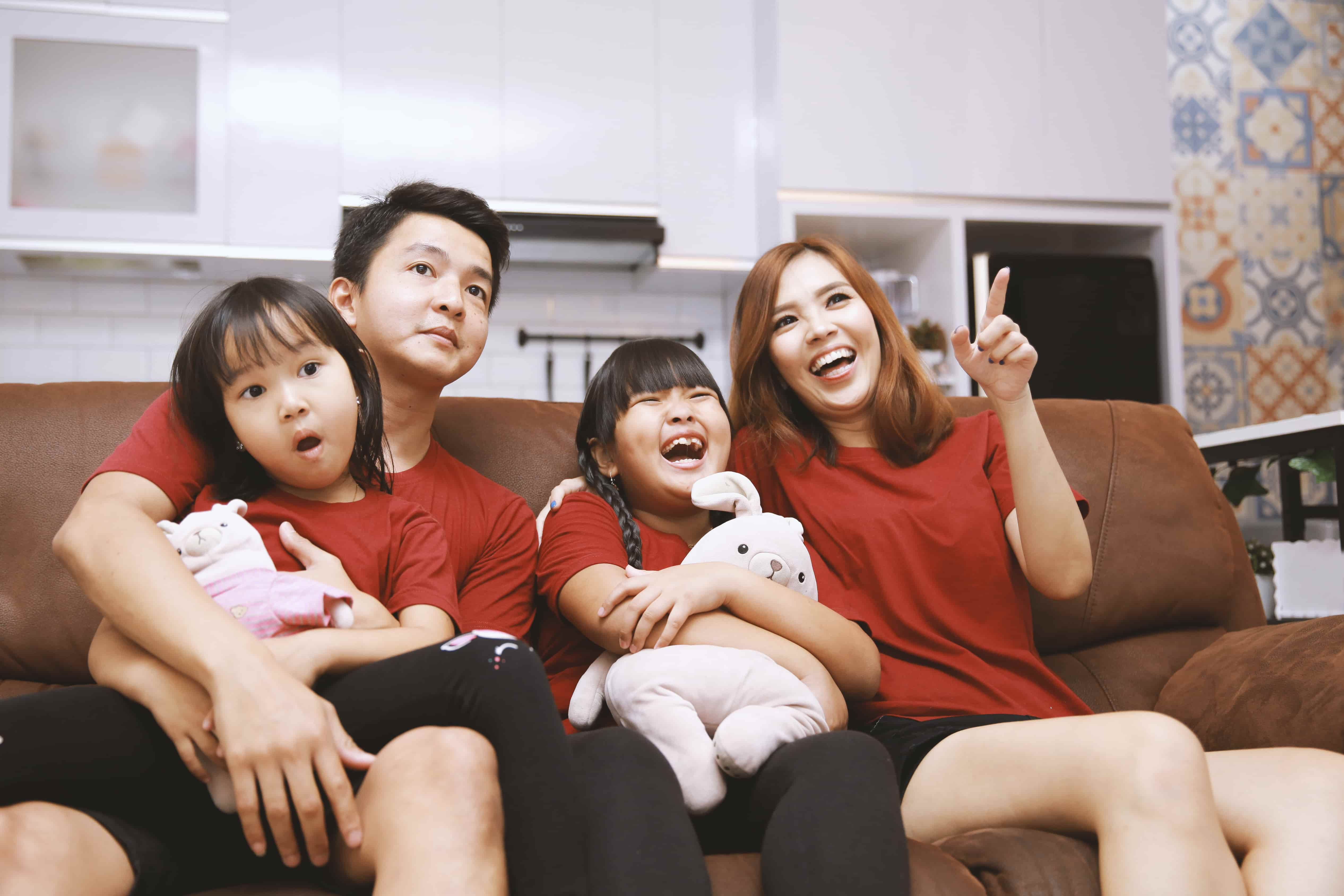 An Asian American family sits on their couch, watching and enjoying a TV program